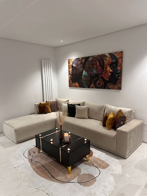 A modern living room with a sectional sofa, a black coffee table with candles, and a large abstract painting on the wall.