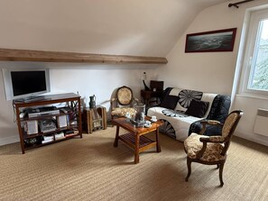 Ein Wohnzimmer mit Fernseher, Holzmöbeln, einem gemusterten Sofa und einem Bild an der Wand.