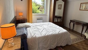 Een slaapkamer met een bed, een nachtkastje met lamp, een raam met gordijnen, een spiegel en een klein tafeltje.