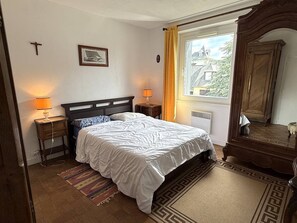 Ein Schlafzimmer mit Bett, Nachttischlampen, einem Fenster mit Vorhängen, einem Heizkörper und einem Holzschrank.