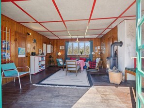 A cozy cabin interior with a wooden floor, a sofa, a dining table, a fireplace, and a window overlooking greenery. - 4 Star Holiday Home in Struer (Struer)