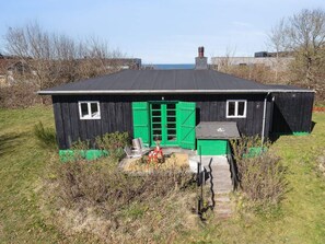 A small black wooden building with green shutters, a chimney, and a small porch with outdoor seating. - 4 Star Holiday Home in Struer (Struer)
