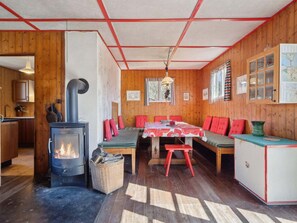 A cozy cabin interior with a central table, red seating, a stove, and wooden walls. - 4 Star Holiday Home in Struer (Struer)