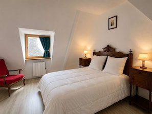 Ein Schlafzimmer mit einem Bett, einem roten Sessel, einem Fenster mit Vorhängen und zwei Nachttischlampen.