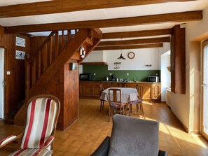 Eine Holztreppe führt zu einer Küche mit grüner Spritzschutzwand, einem Esstisch mit Stühlen und einem gestreiften Sessel.