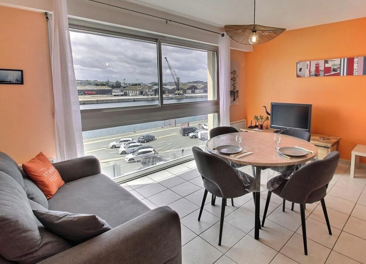 A modern living room with a large window, a dining table, and a television.