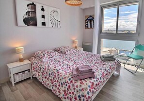 Ein Schlafzimmer mit Bett, Nachttisch, Stuhl, Fenster mit Aussicht und Wandbildern.