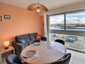 Ein modernes Zimmer mit rundem Tisch, einer Couch, einer Lampe und einem großen Fenster mit Blick auf einen Hafen und Gebäude.