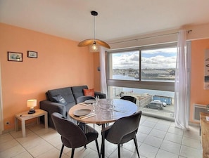 Ein modernes Wohnzimmer mit einem runden Esstisch, einem grauen Sofa und einem großen Fenster mit Stadtblick.