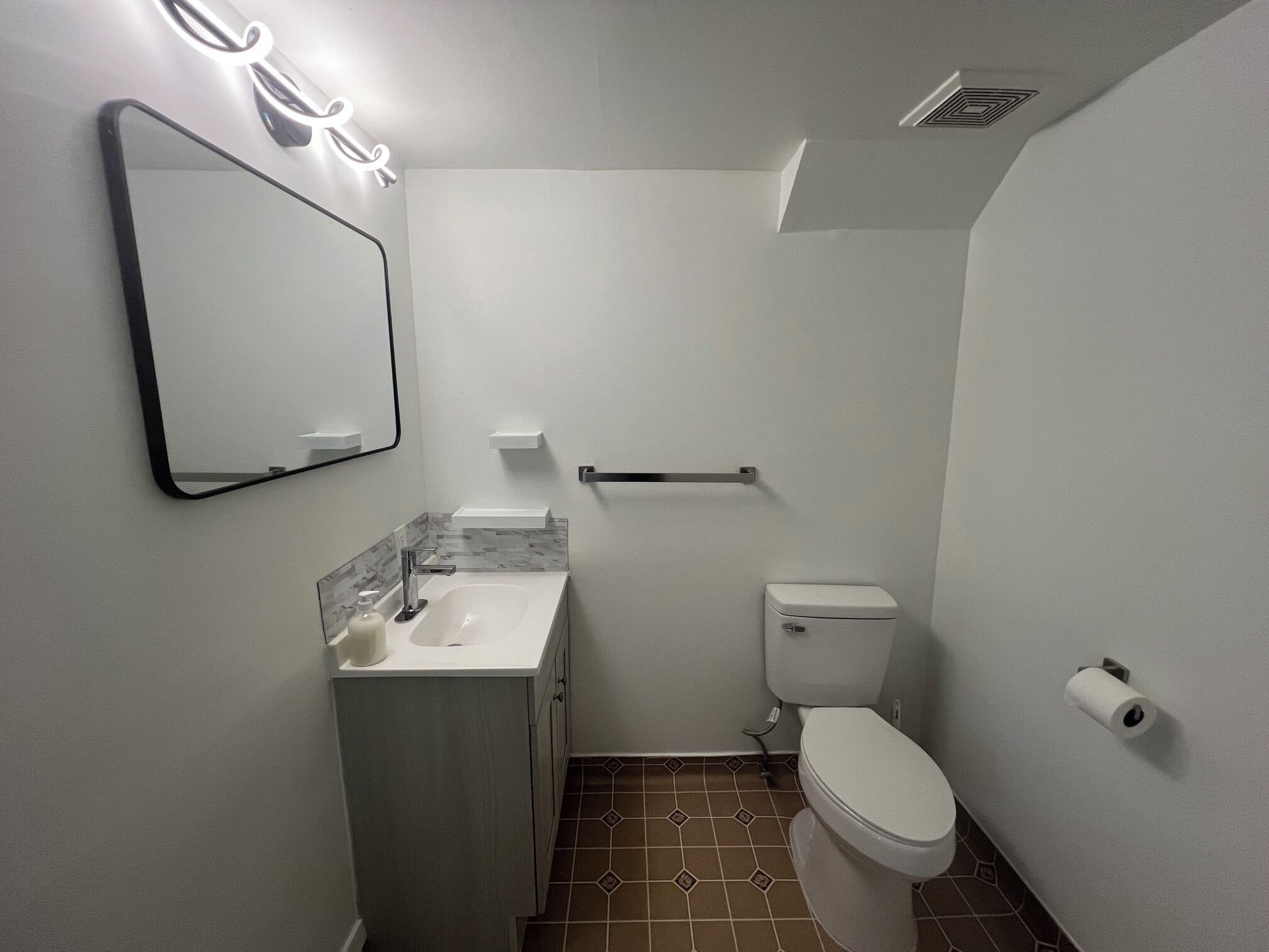 A bathroom with a sink, mirror, toilet, and towel rack.