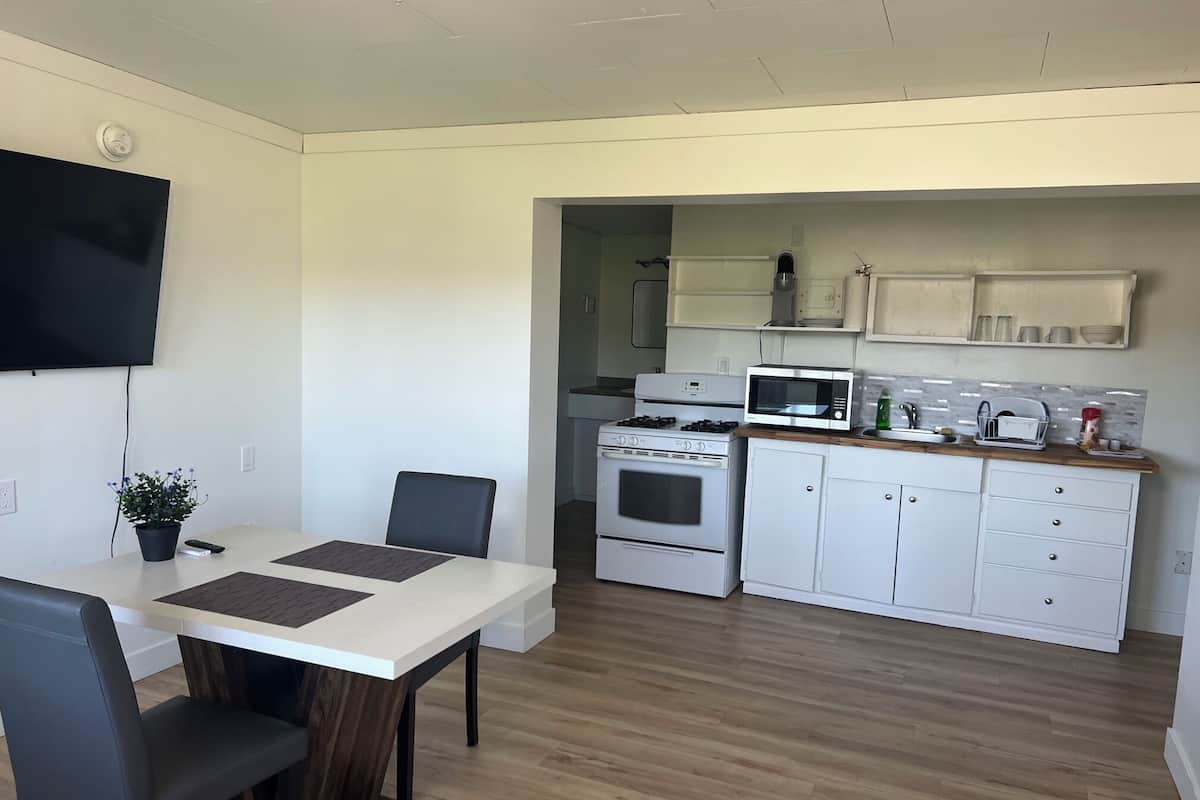 A modern kitchen with white cabinets, a microwave, stove, and a dining area with a table and chairs.