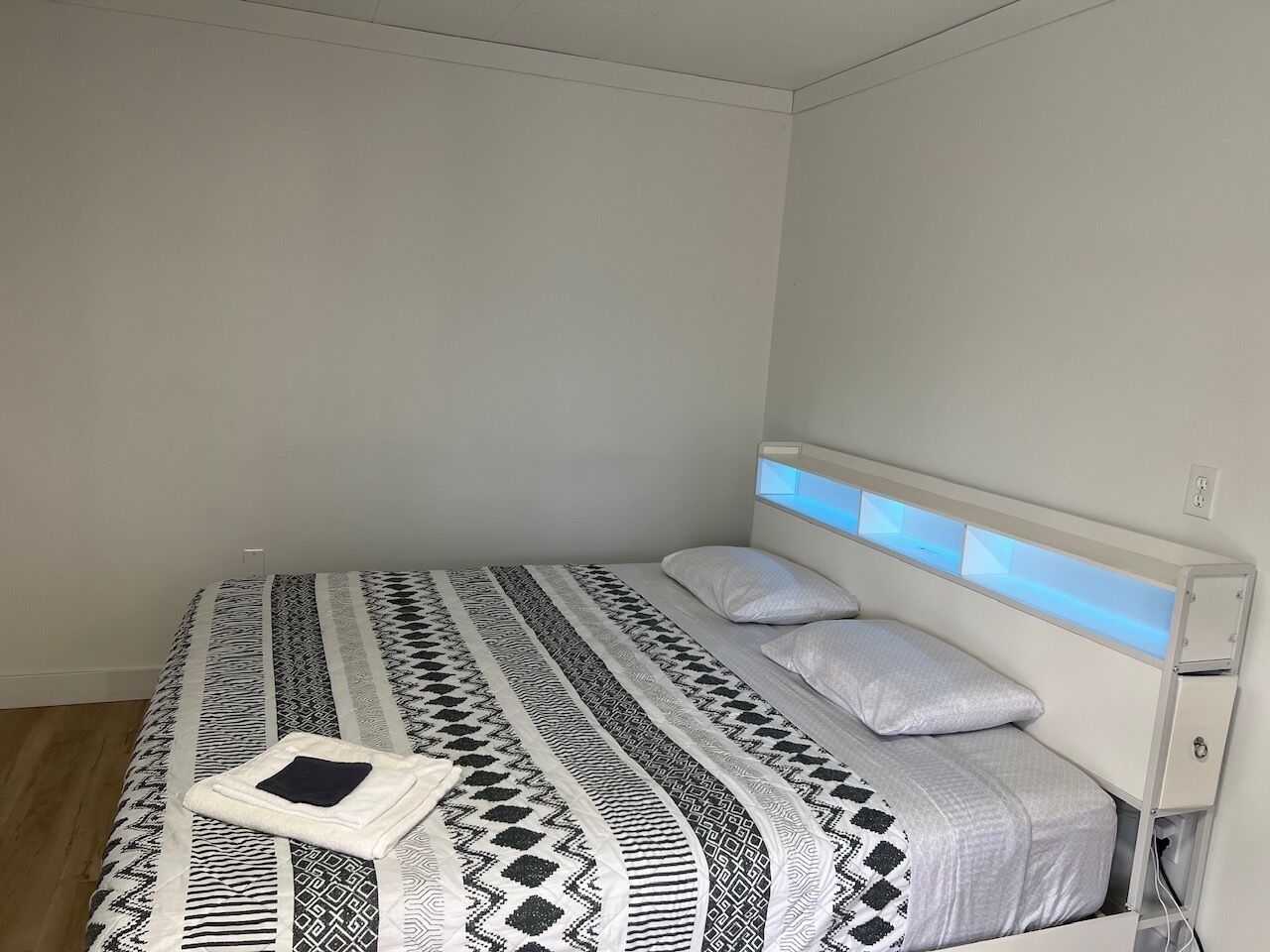 A single bed with a patterned bedspread and pillows, a bedside table, and a wall-mounted light fixture.
