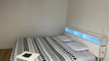 A single bed with a patterned bedspread and pillows, a bedside table, and a wall-mounted light fixture.