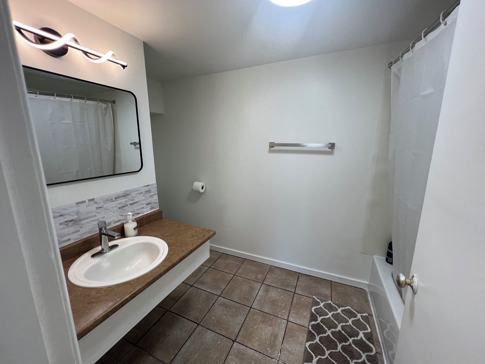 Un bagno con lavandino, specchio, porta asciugamani e tenda per la doccia.