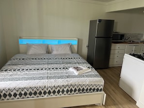 Un dormitorio con cama, refrigerador, microondas y una zona de cocina.