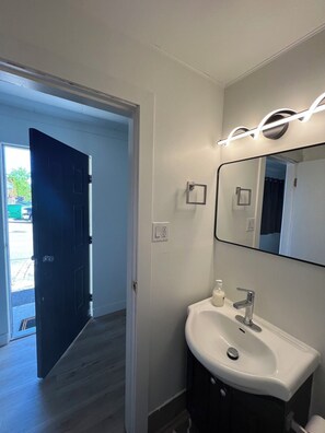 A bathroom with a white sink, a mirror, and a door leading to a hallway.