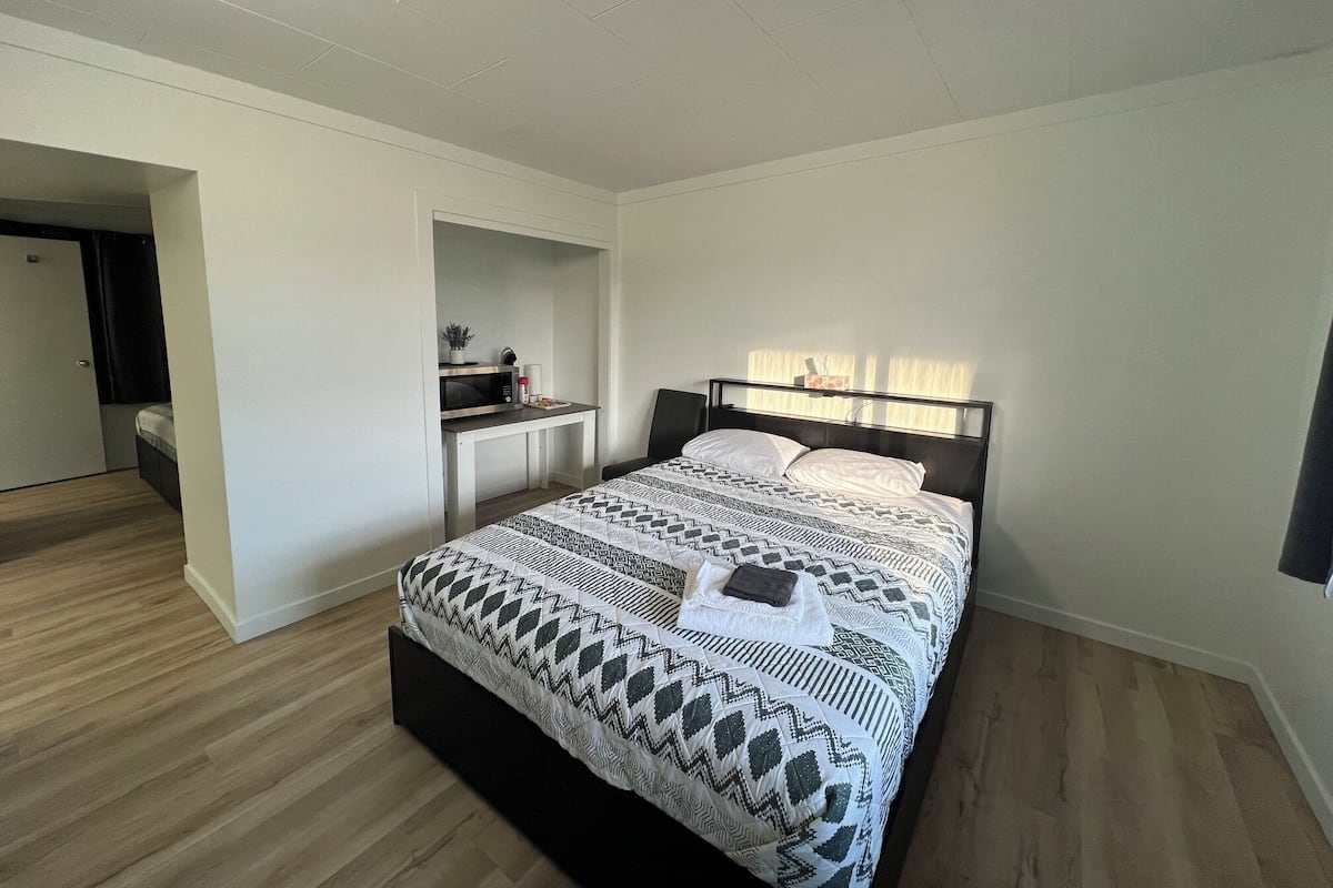 A bedroom with a bed, a desk, and a small kitchenette.