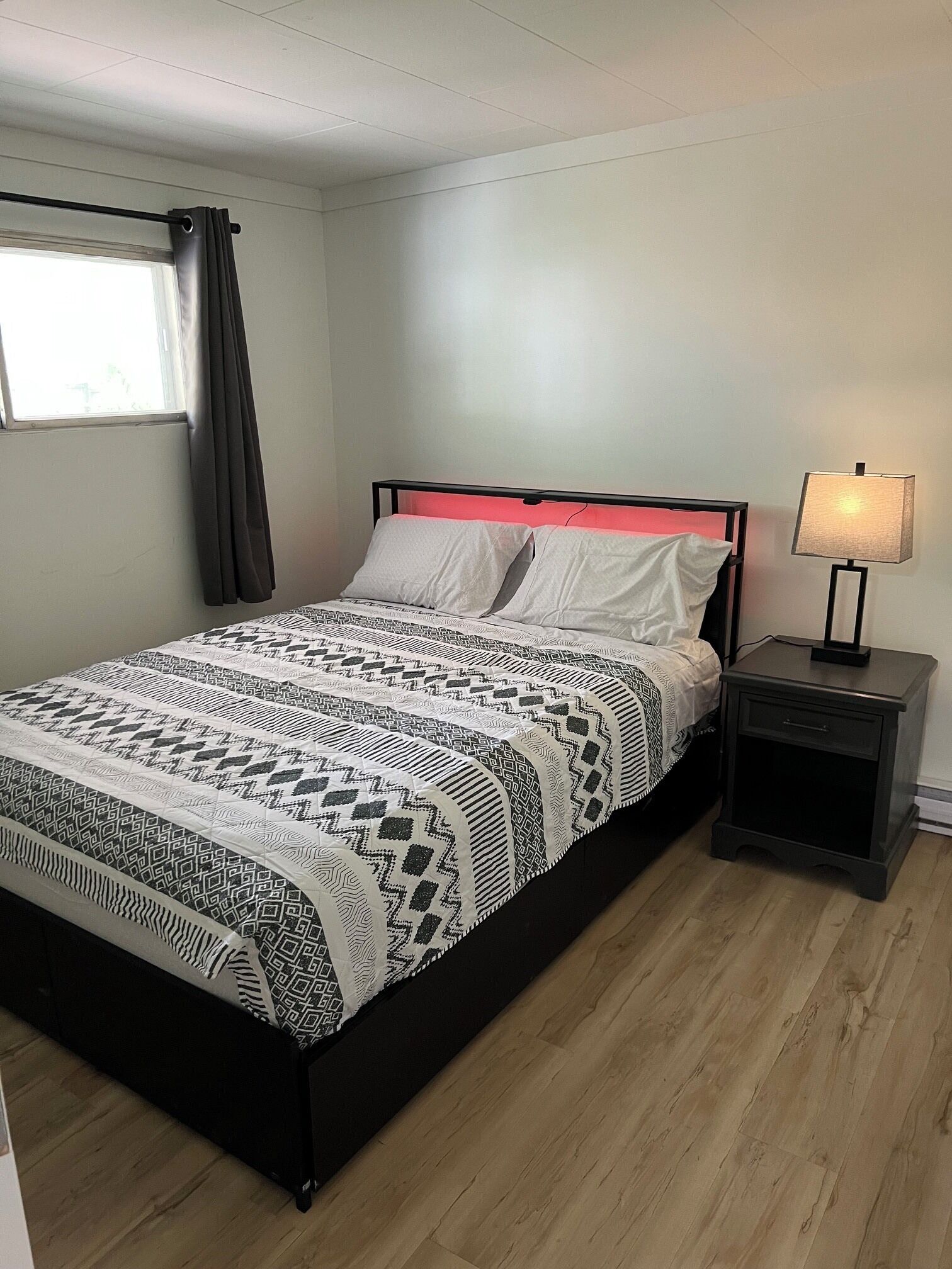 Un lit avec une couvre-lit à motifs, une table de chevet avec une lampe et une fenêtre avec des rideaux.