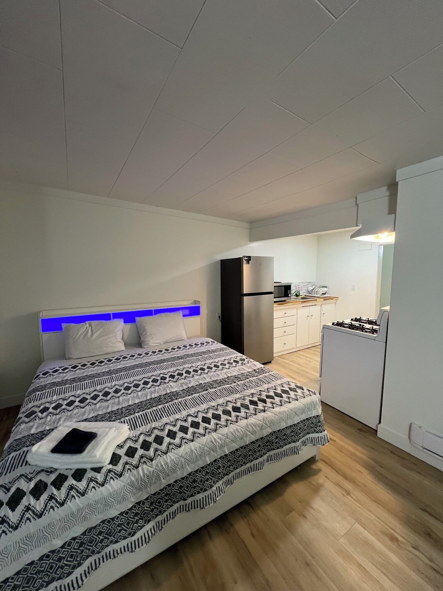A bedroom with a bed, a bedside table, a built-in wardrobe, and a kitchenette area with a stove and refrigerator.