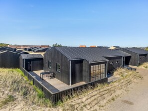 A row of modern, black-roofed cabins with wooden decks and large windows, surrounded by sand dunes and sparse vegetation. - "Raimund" - 600m from the sea by Interhome (Løkken)