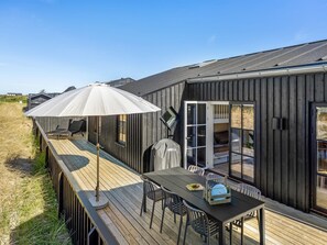 A wooden deck with a table and chairs, a covered umbrella, and a sliding glass door leading to a bedroom. - "Raimund" - 600m from the sea by Interhome (Løkken)