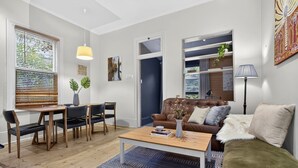A modern living room with a brown leather sofa, a wooden coffee table, and a dining area with a table and chairs. - Ada Art Deco by Host Solutions Hutt St, Heritage (Adelaide)