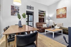 Ein modernes Wohnzimmer mit Esstisch, Ledersesseln, einem braunen Sofa, einem Couchtisch und Kunstwerken an den Wänden.