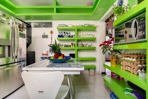 A kitchen with green shelves, a bowl of fruit, and a refrigerator.