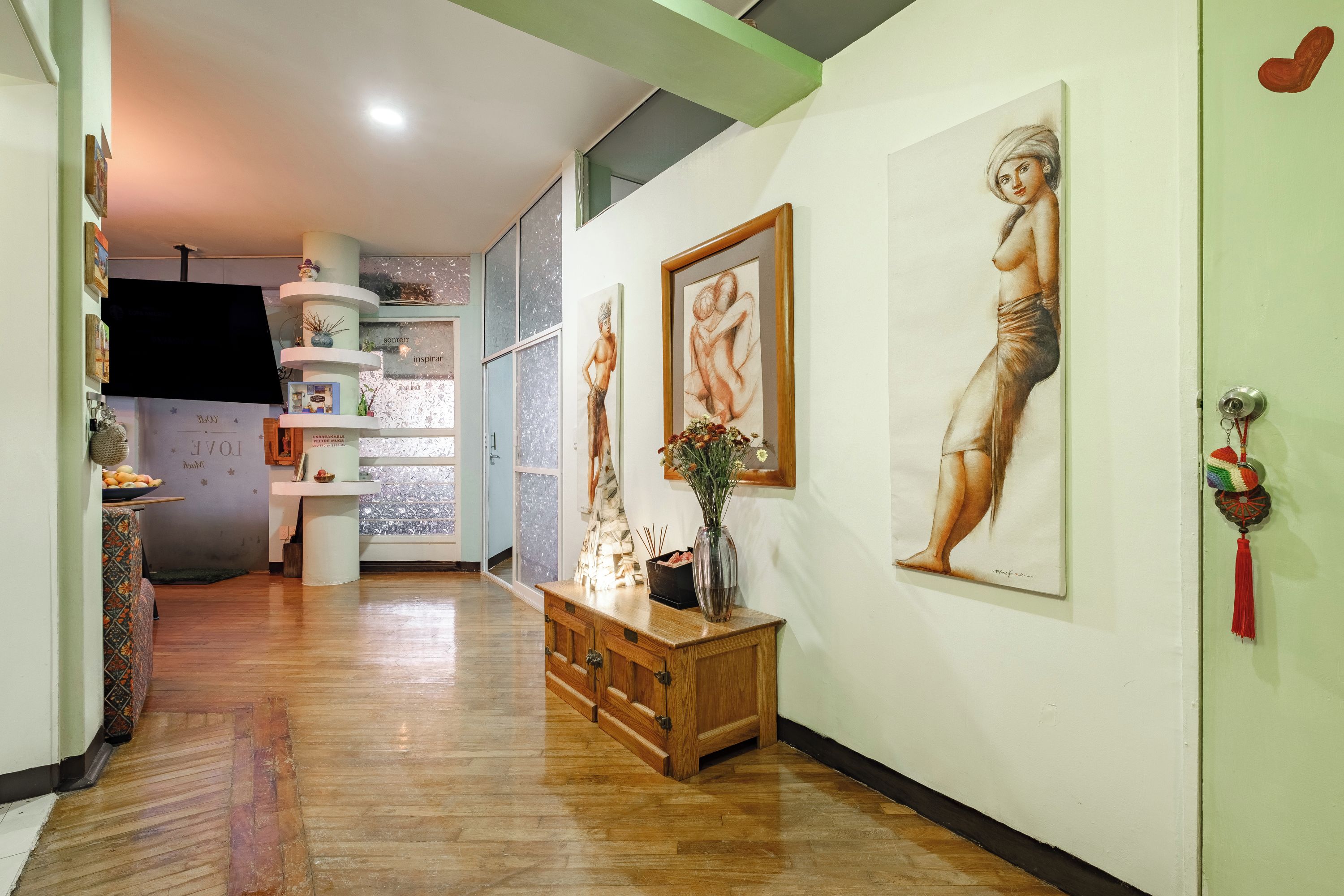Um corredor com piso de madeira, um console de madeira com um vaso e duas obras de arte emolduradas na parede.