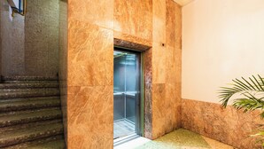 A marble staircase leading to an elevator, a potted plant, and a wall with a light fixture. - Hostal Itzae Polanquito (Mexico City)