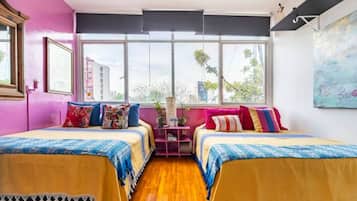 Una habitación con dos camas, ventanas amplias, una pared rosa y un cuadro.