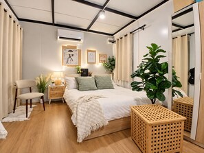 Une chambre à coucher moderne avec un grand lit, des tables de chevet, une chaise, une plante en pot et une petite table en bois.