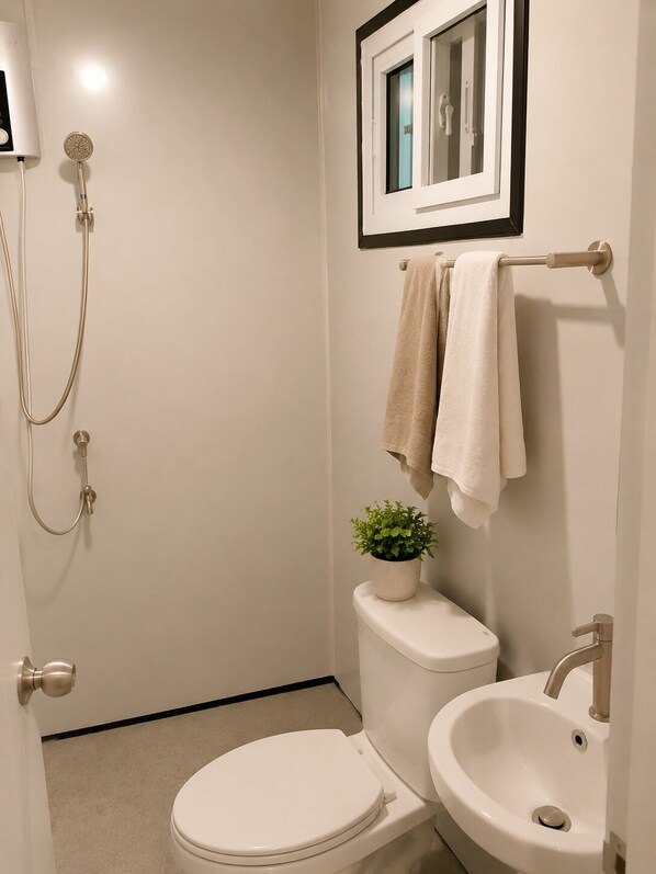 A bathroom with a toilet, bidet, sink, shower, and a framed picture above the mirror.