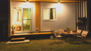 Un espace extérieur moderne et bien éclairé, aménagé avec des sièges et offrant une vue sur l’intérieur.