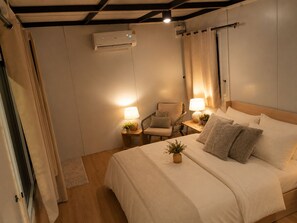 Ein Schlafzimmer mit einem Bett, zwei Nachttischen mit Lampen, einem Sessel und einer Klimaanlage.