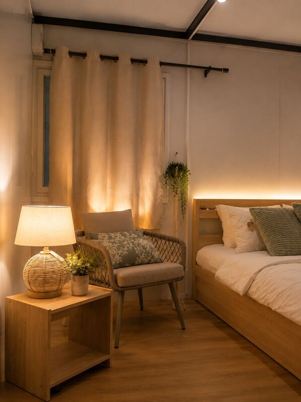 A bedroom with a wooden nightstand, a lamp, a wicker chair, and a bed with pillows.