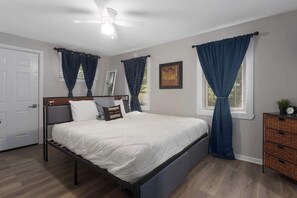 A bedroom with a bed, a dresser, a ceiling fan, and a window with curtains. - 3BR One Level Ranch home + Easy Hwy Access (Kansas City)