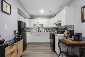 A modern kitchen with white cabinets, a black stove, and a tiled backsplash. - 3BR One Level Ranch home + Easy Hwy Access (Kansas City)