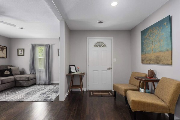 A living room with a grey sofa, a brown armchair, a small table, and a door with a decorative glass panel. - 3BR One Level Ranch home + Easy Hwy Access (Kansas City)