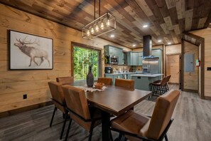 A wooden interior with a dining table, chairs, a kitchen area, and a framed animal picture. - Timber Vail | Luxury Cabin in the Woods (Sevierville)