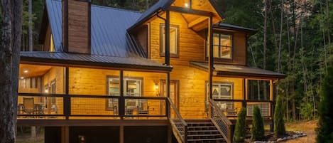 A two-story wooden cabin with a balcony, a covered porch, and a staircase leading to the upper level.