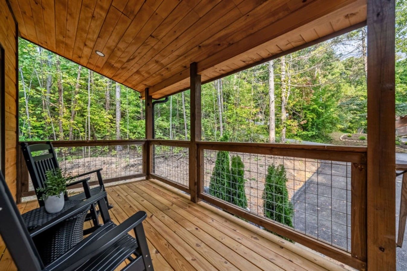 A wooden deck with a view of a forest, a bench, and a table.