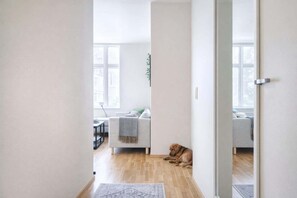 A room with a wooden floor, a sofa, a dog, and a door leading to another room. - Modern Apartment, Panoramic View in Heart of Bergen (Bergenhus)