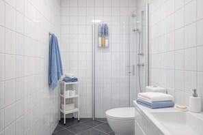 A small, modern bathroom with white tiles, a glass shower enclosure, a toilet, and a white sink with a soap dispenser. - Modern Apartment, Panoramic View in Heart of Bergen (Bergenhus)