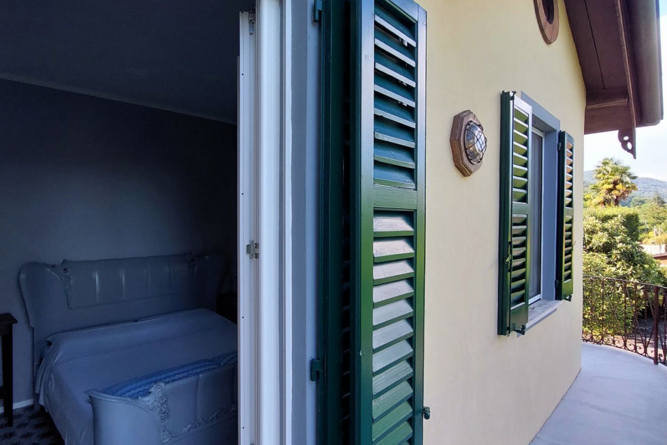 Ein Zimmer mit einem Bett, einem Fenster mit grünen Rollläden und einem Balkon mit Geländer.