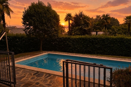 A swimming pool with a stone deck, surrounded by greenery and palm trees, with a sunset in the background.. Acquazzurra, luxury duplex, pool, parking space, free WiFi