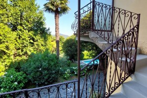 A wrought iron balcony railing, a stone staircase, lush greenery, and a pool. - Acquazzurra, luxury duplex, pool, parking space, free WiFi (Lesa)