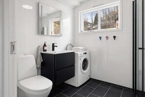 Et moderne badeværelse med toilet, vask, vaskemaskine og et vindue med udsigt.