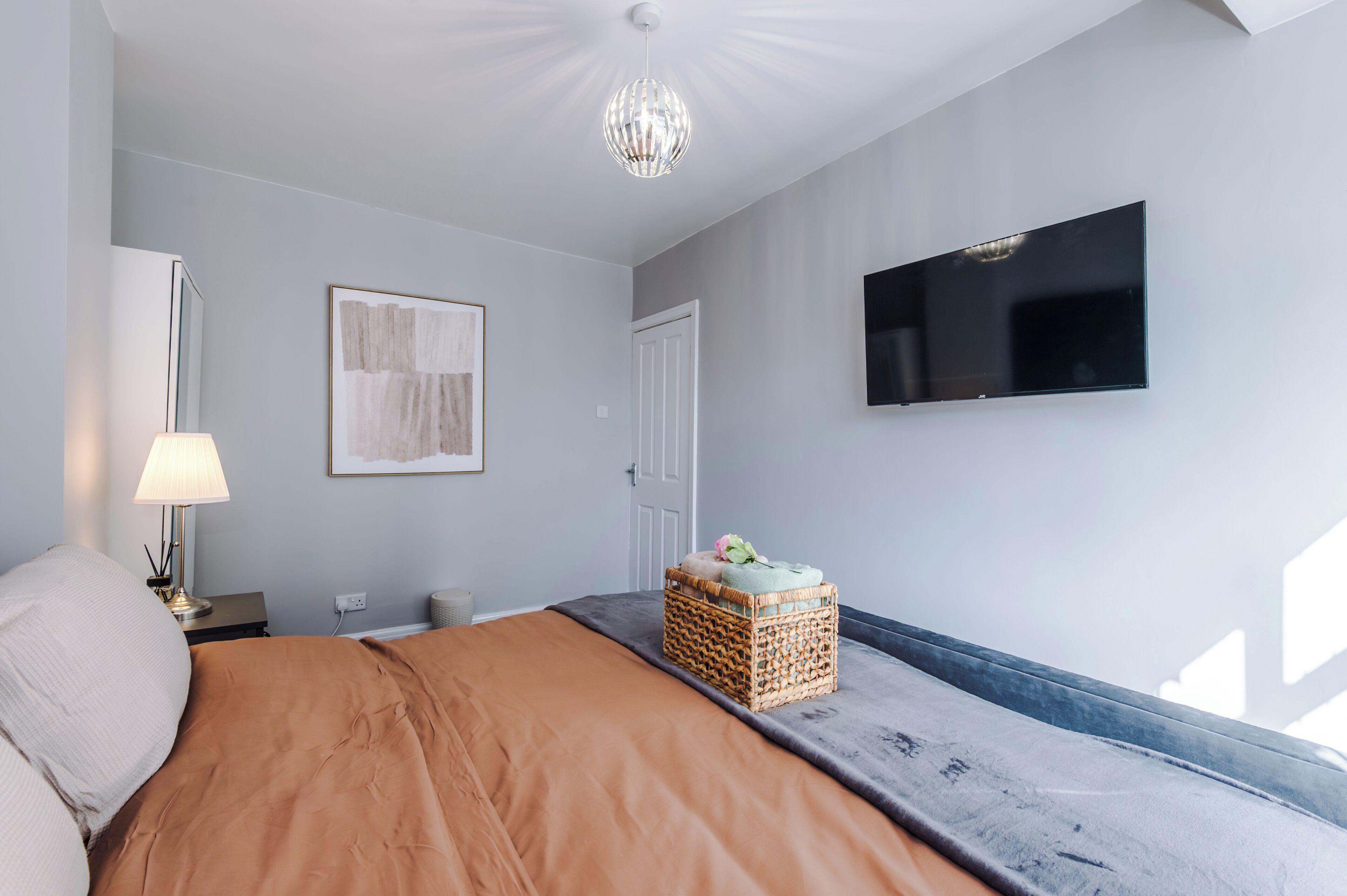 A bedroom with a bed, a television mounted on the wall, a lamp, and a framed artwork.