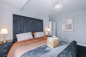 Un dormitorio con cama, lámparas de noche, cabecero, mesita de noche, una obra de arte en la pared y una lámpara de pie.